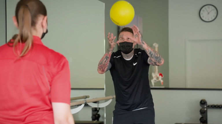 physical therapist works on movement with patient by playing catch