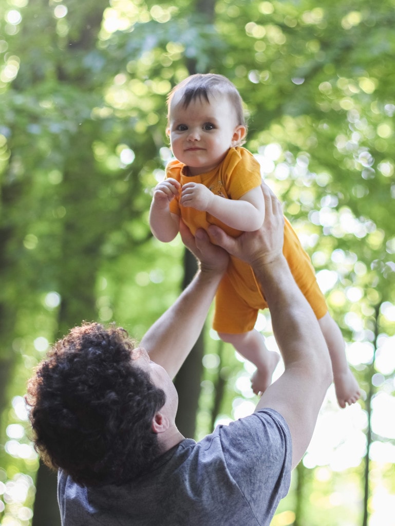 infant child looks as she is held up high above dad's head