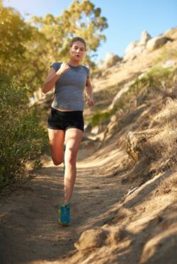 fit woman runs downhill on trail