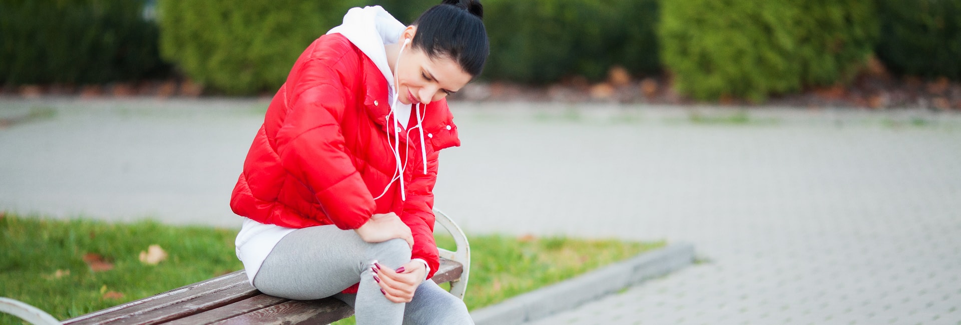 woman holds her knee in pain while sitting outdoors on a cool day after a workout