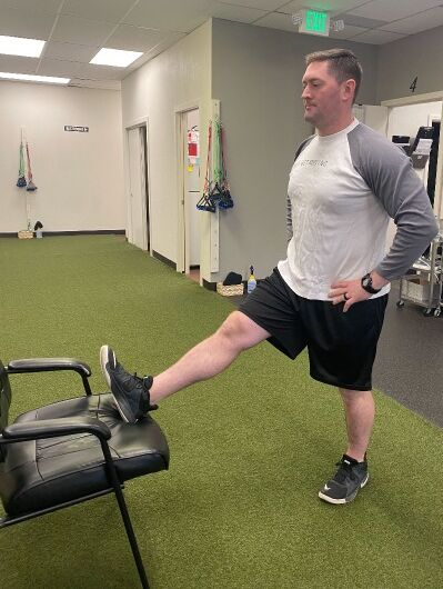 demonstrating standing hamstring stretch with a chair