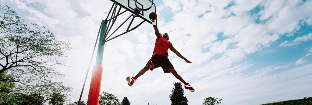 man on outdoor basketball court jumps high to the hoop for a shot